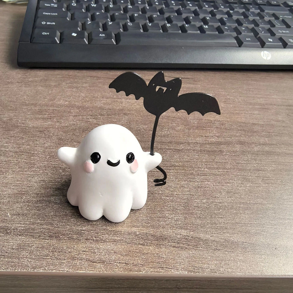 Mini resin Halloween statue of a white ghost dog walking and holding a small black bat.