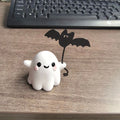 Mini resin Halloween statue of a white ghost dog walking and holding a small black bat.