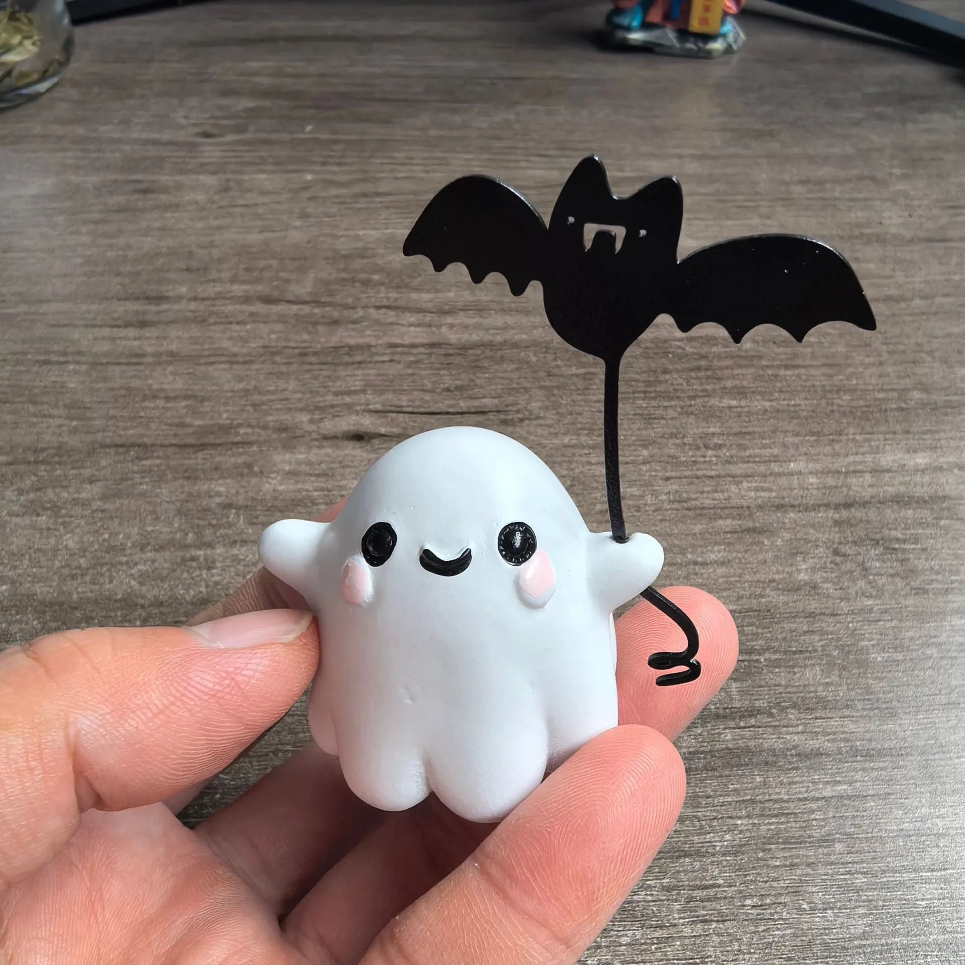 Mini resin Halloween statue of a white ghost dog walking and holding a small black bat.