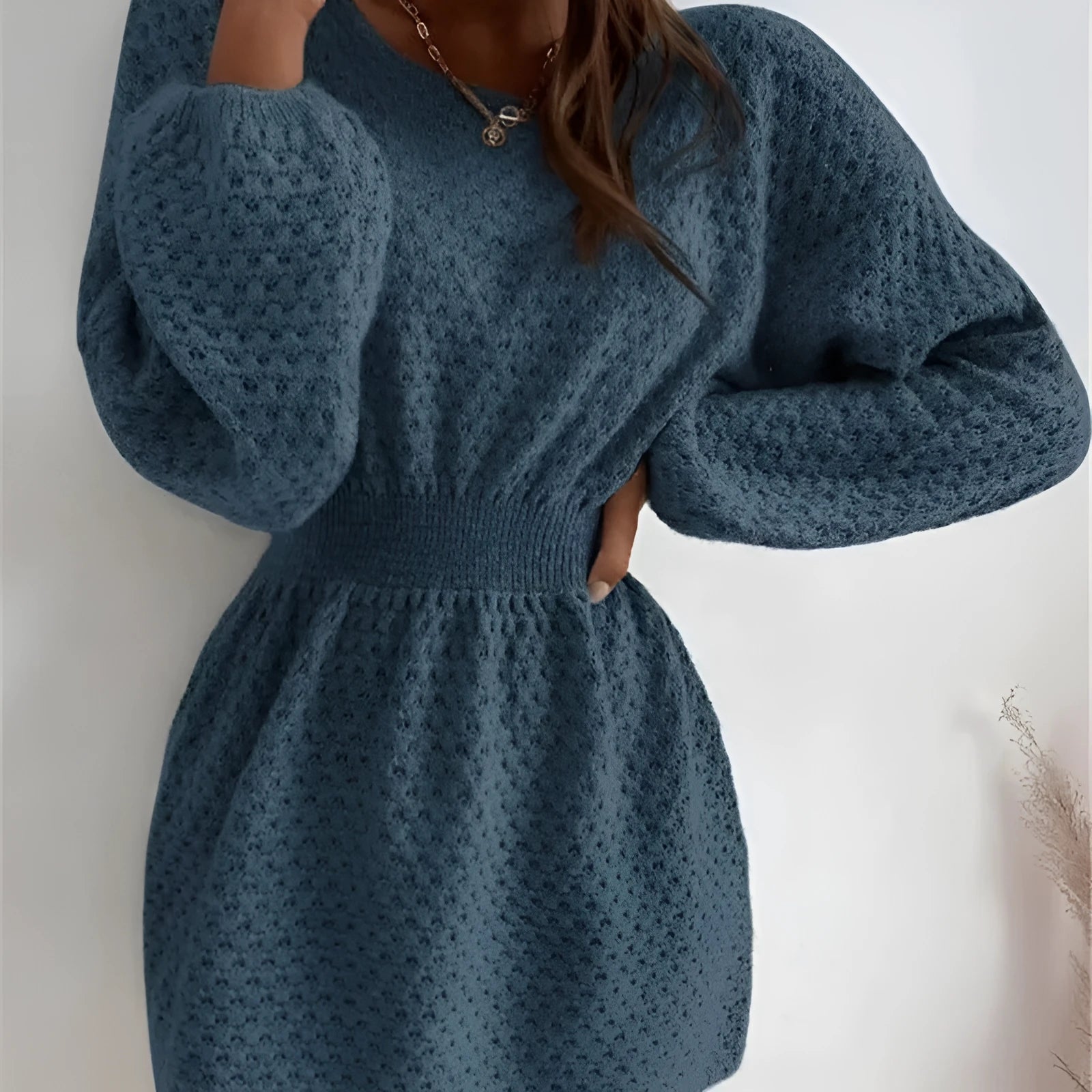 Blue knitted dress with fitted waist, round neck, long sleeves, and white crocheted flower details.