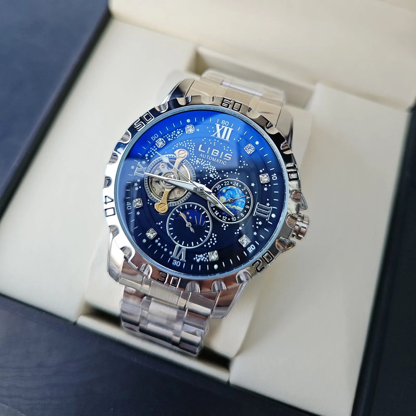 Men's silver automatic watch with black starry dial and leather strap on wrist.