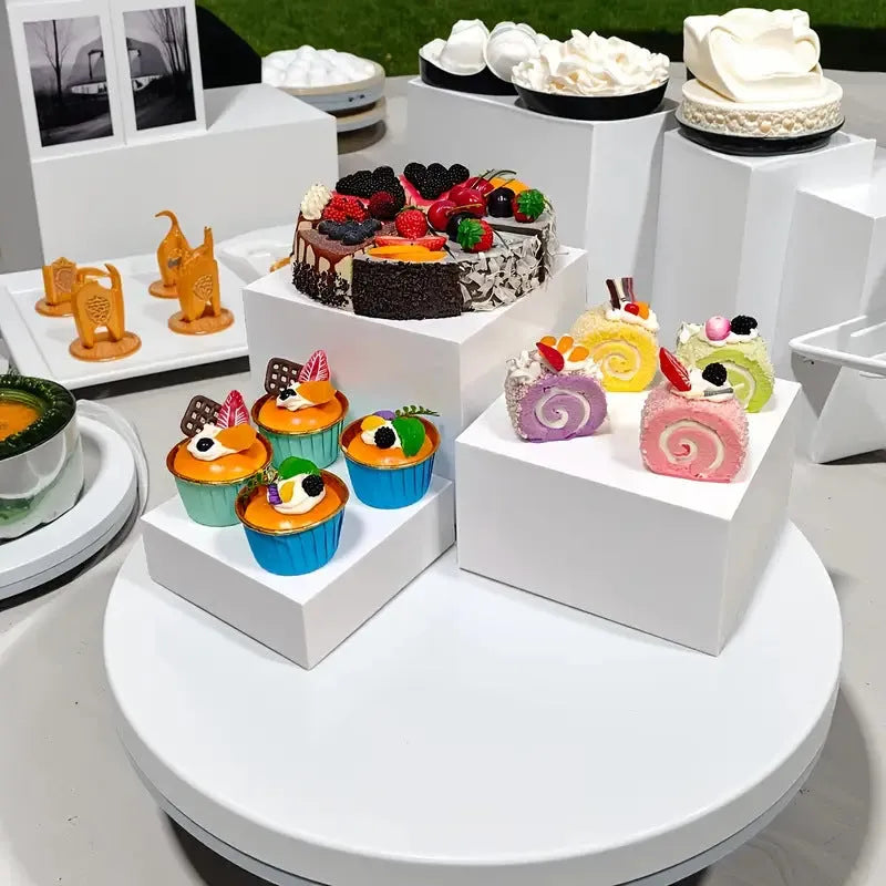 Set of six white plastic dessert display stands arranged on a tabletop.