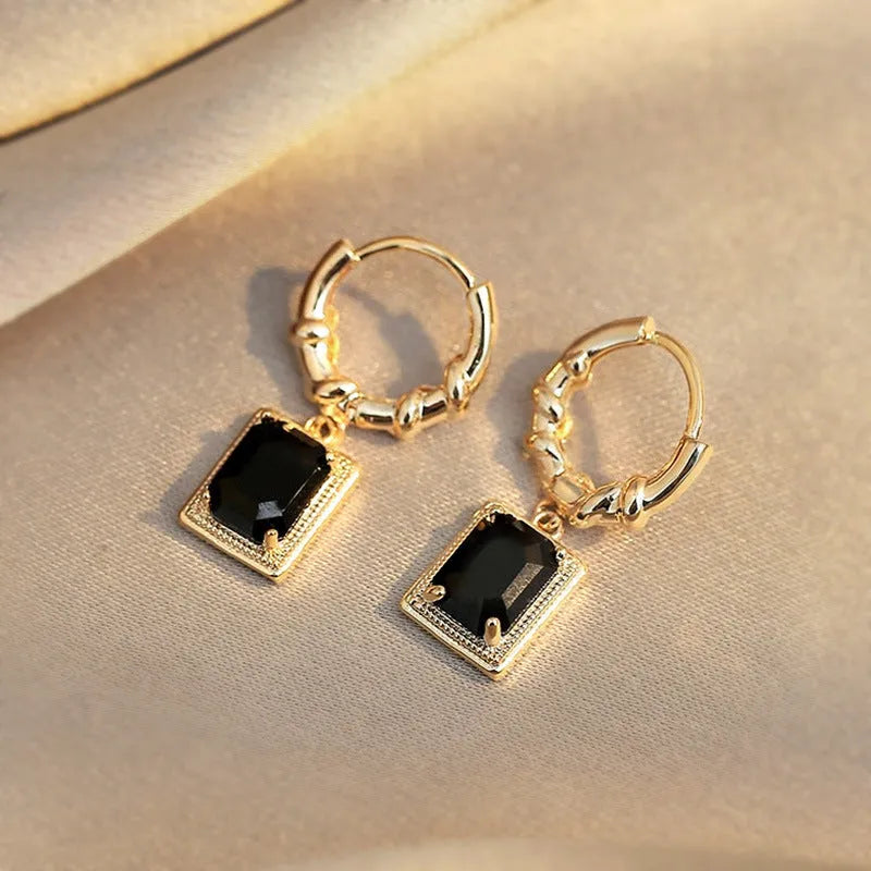 Close-up of women's geometric quadrilateral copper drop earrings with multiple black zircon stones on a grey background.
