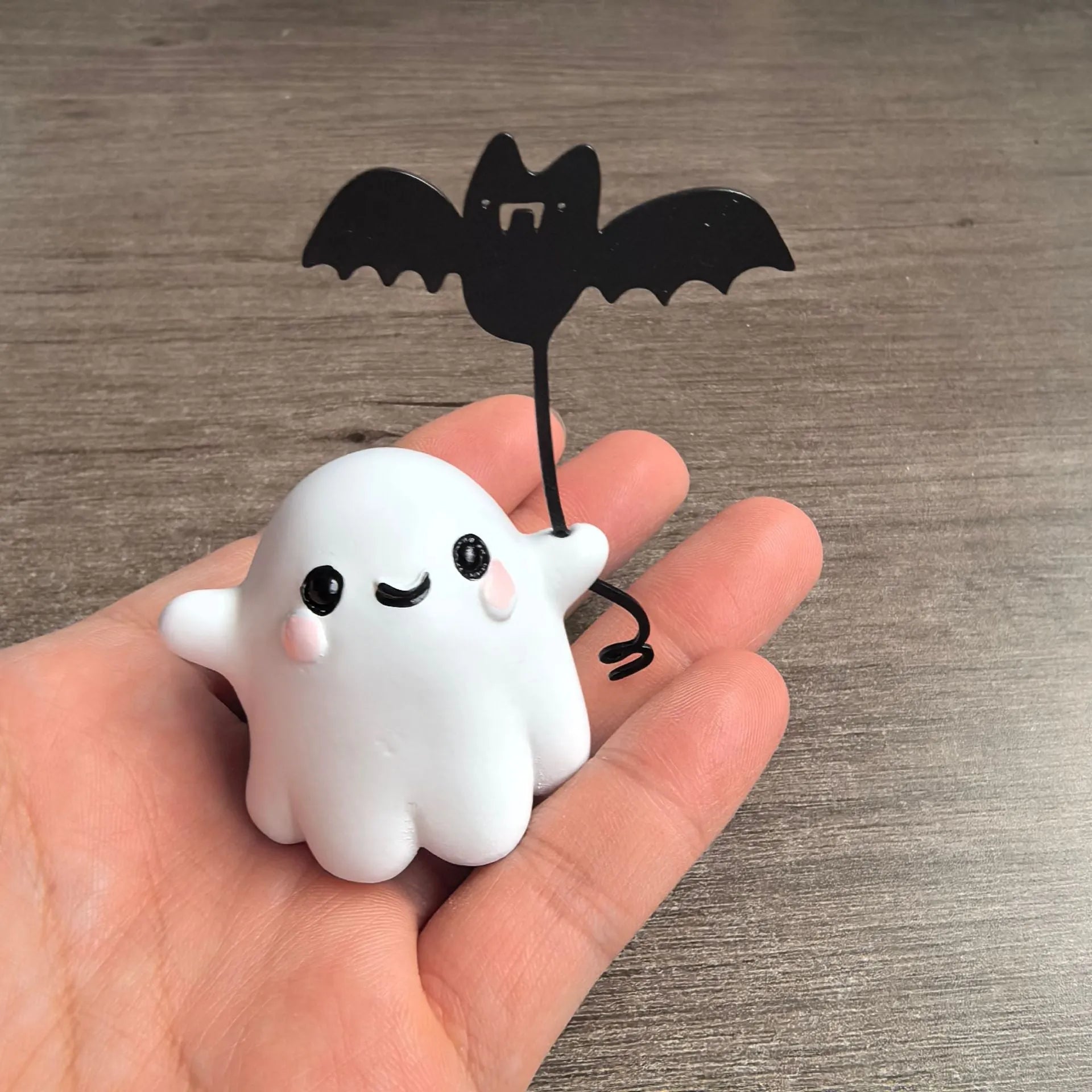 Mini resin Halloween statue of a white ghost dog walking and holding a small black bat.