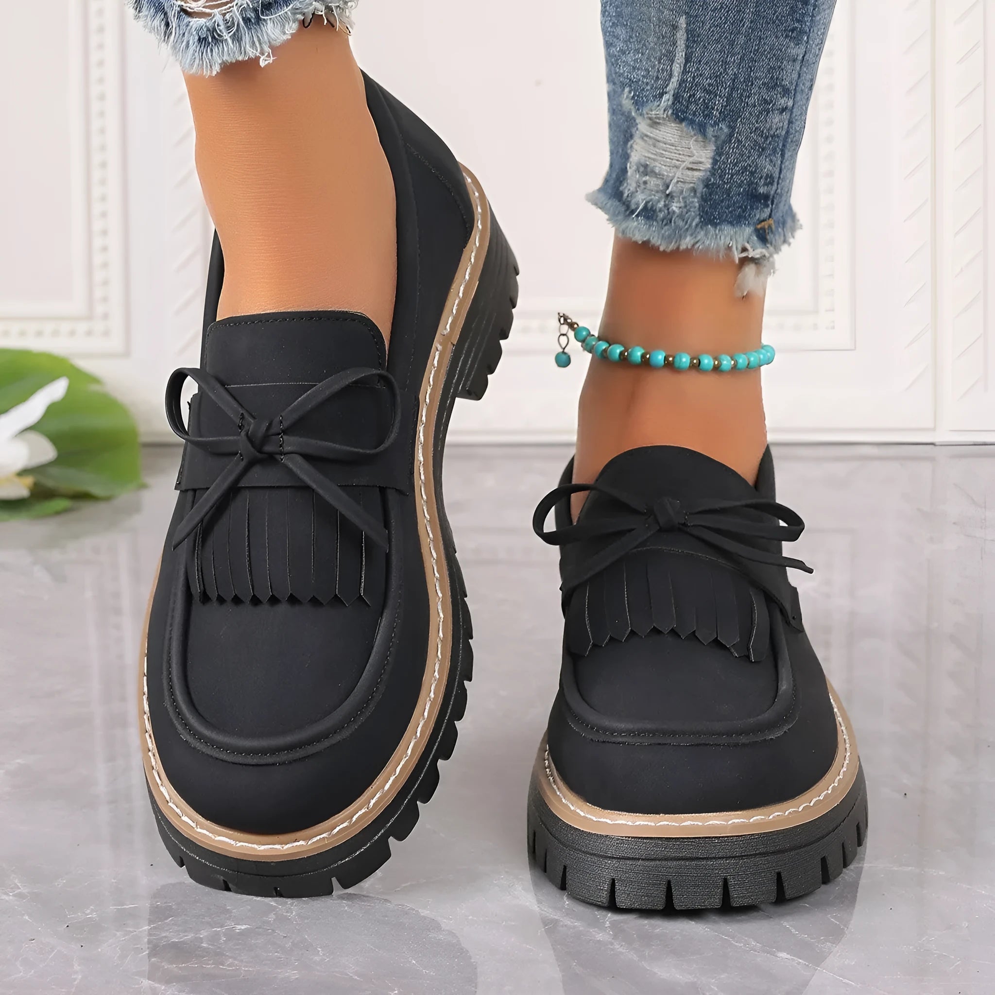 Women's black loafers with a tassel and bow detail on a chunky rubber sole.
