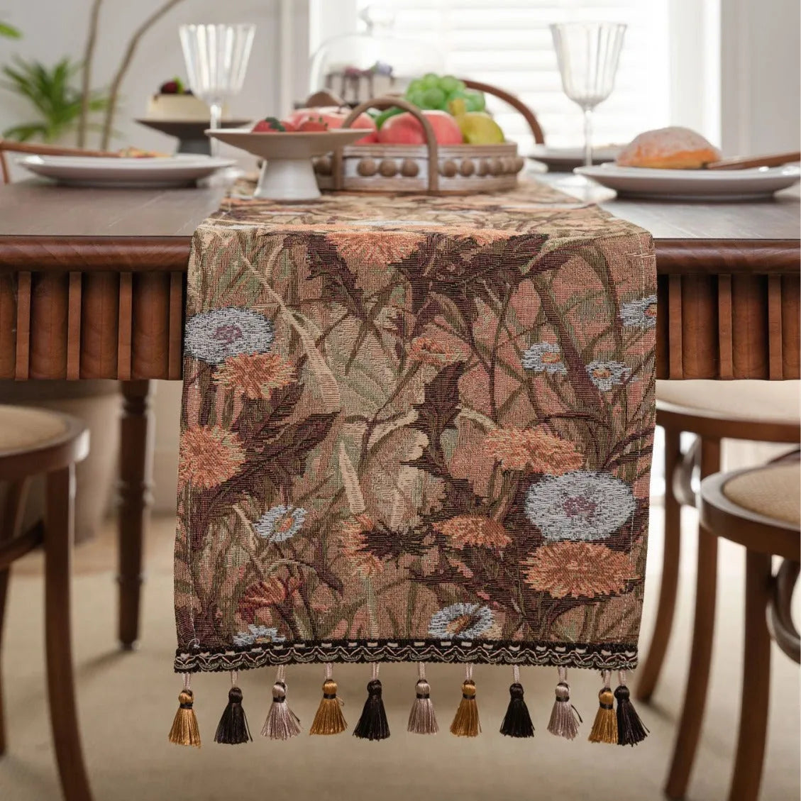 Long beige jacquard table runner with floral pattern and tassels draped on a wooden dining table.
