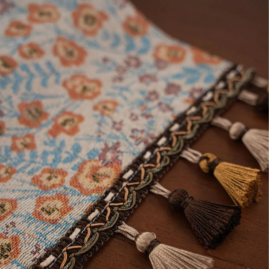 Long beige jacquard table runner with floral pattern and tassels draped on a wooden dining table.