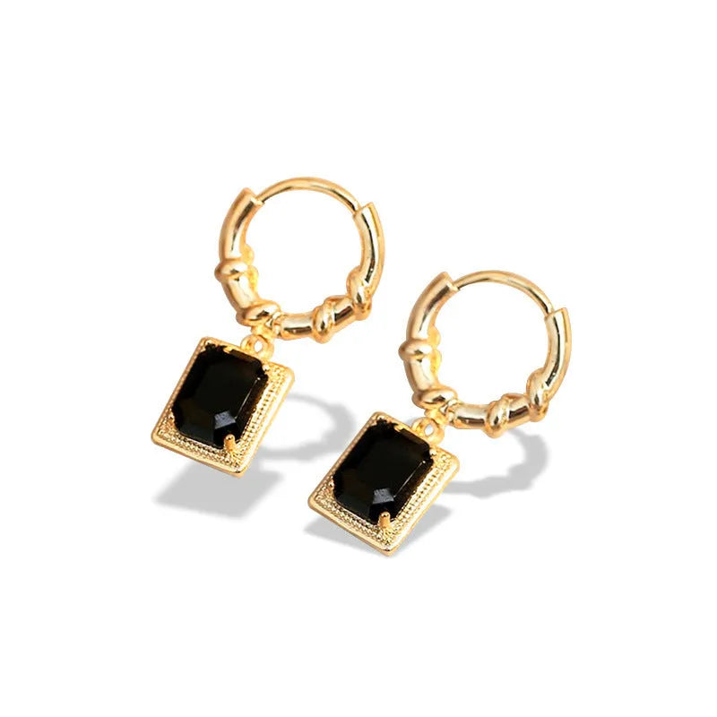 Close-up of women's geometric quadrilateral copper drop earrings with multiple black zircon stones on a grey background.