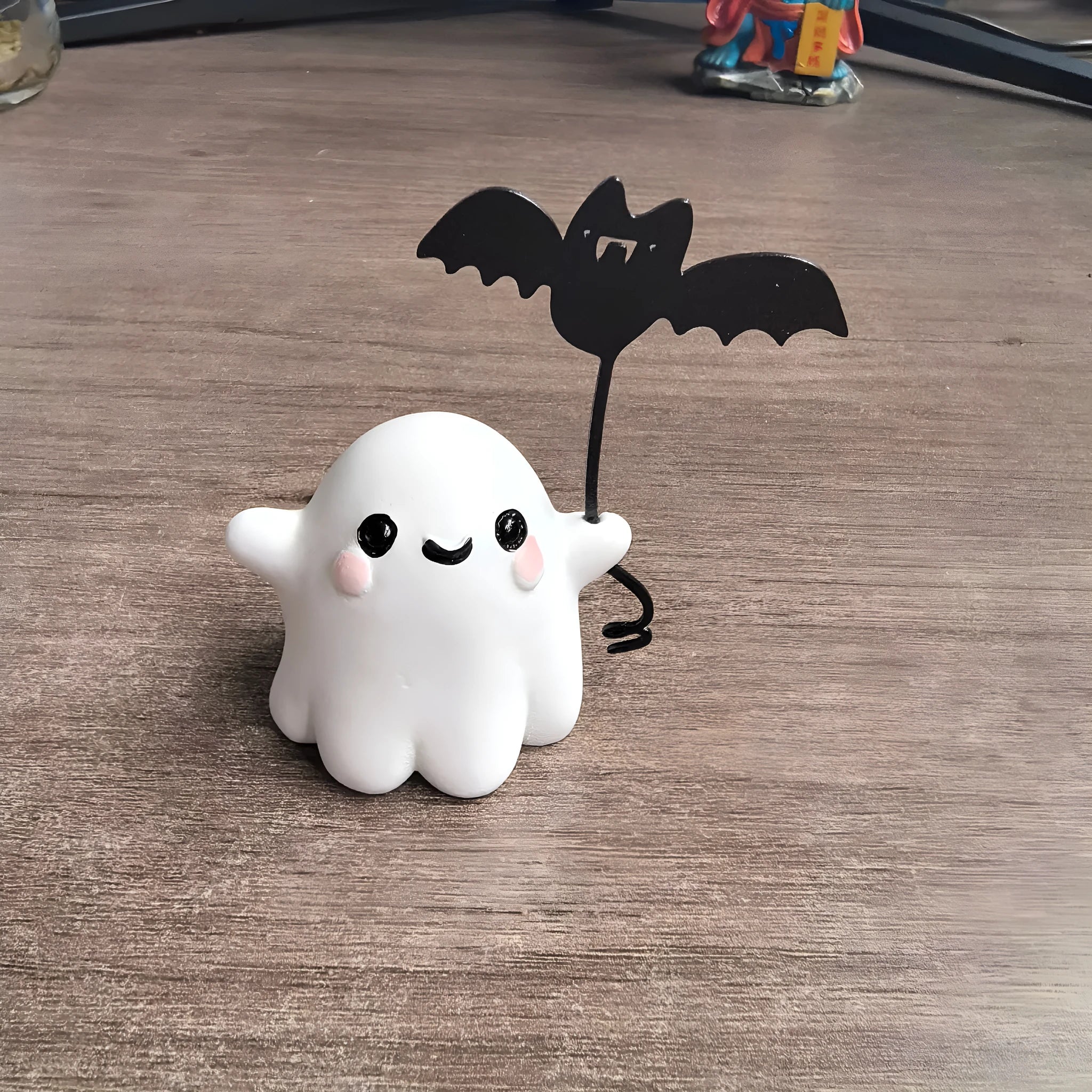 Mini resin Halloween statue of a white ghost dog walking and holding a small black bat.