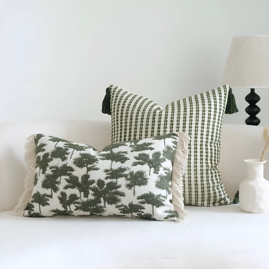 Green striped and botanical patterned pillow with beaded fringe on a bed.