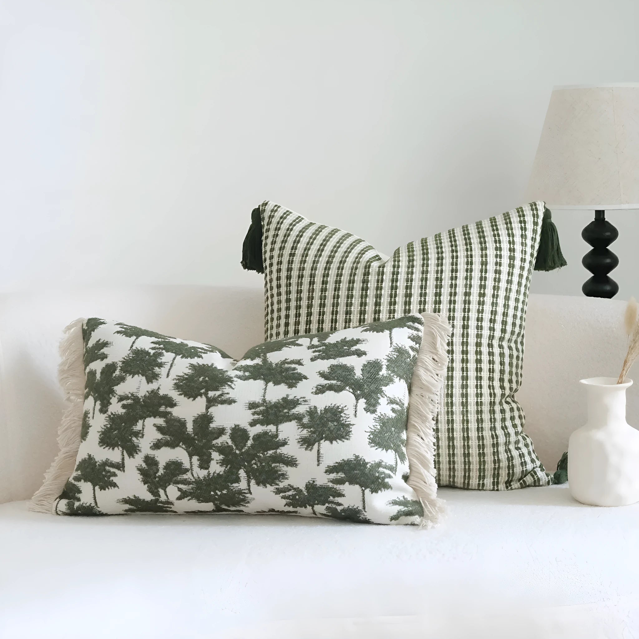 Green striped and botanical patterned pillow with beaded fringe on a bed.