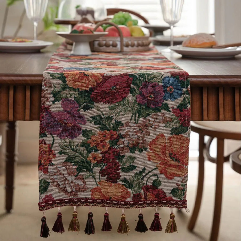 Long beige jacquard table runner with floral pattern and tassels draped on a wooden dining table.