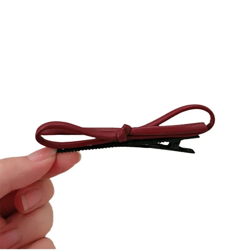 Wine red genuine leather bow hair barrette with a silver metal pinch clip on a white background.