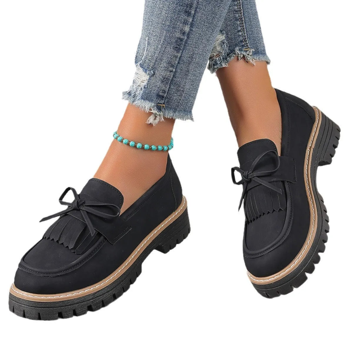 Women's black loafers with a tassel and bow detail on a chunky rubber sole.