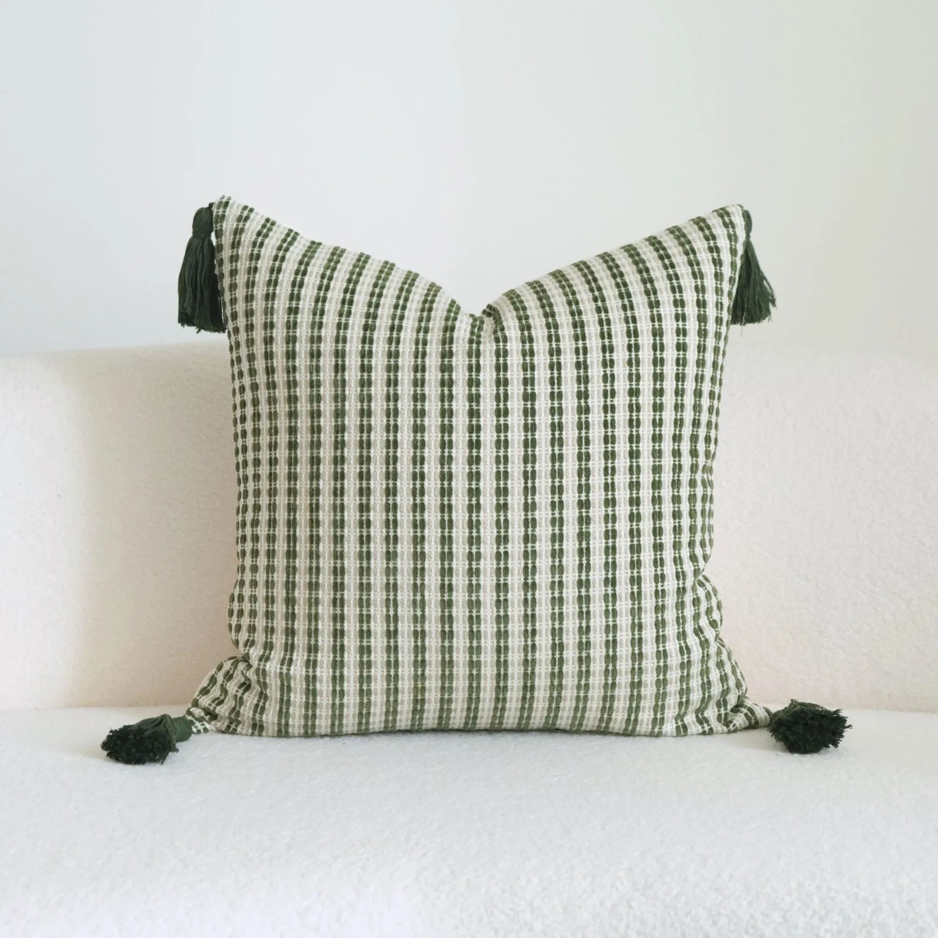 Green striped and botanical patterned pillow with beaded fringe on a bed.