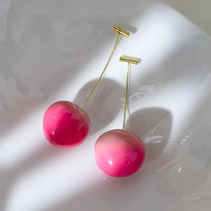 Close-up of a pair of peach-shaped acrylic earrings on a woman's ear, showing the small and large size options.