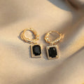Close-up of women's geometric quadrilateral copper drop earrings with multiple black zircon stones on a grey background.