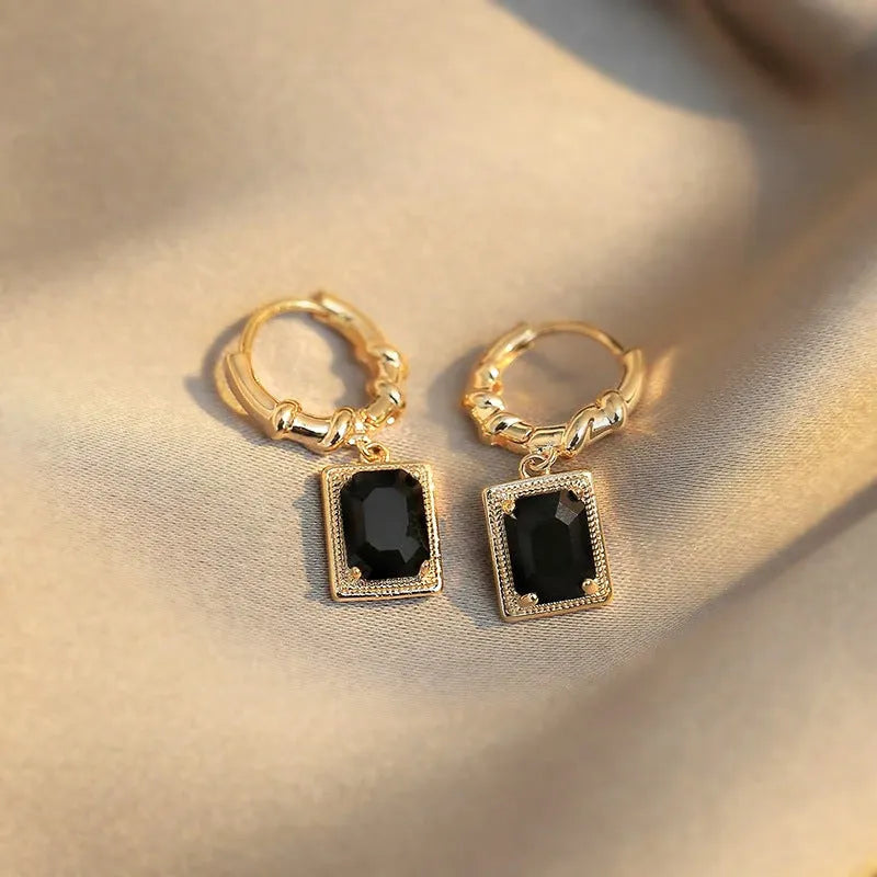 Close-up of women's geometric quadrilateral copper drop earrings with multiple black zircon stones on a grey background.