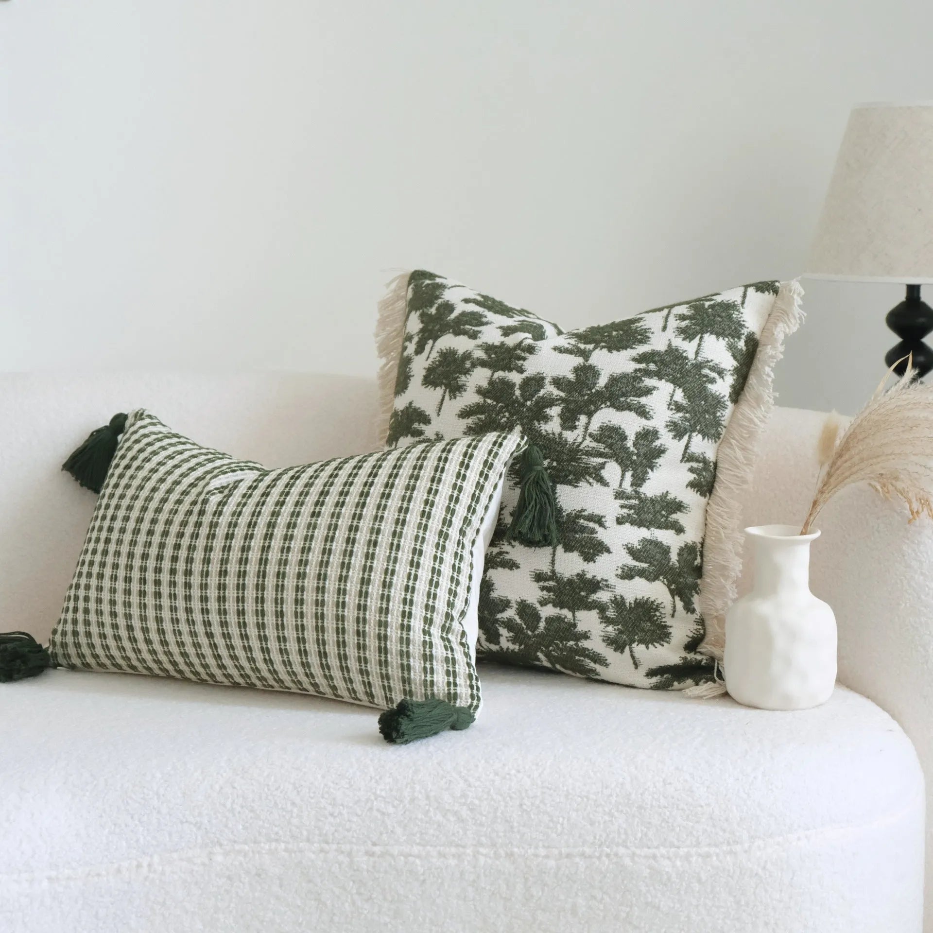 Green striped and botanical patterned pillow with beaded fringe on a bed.
