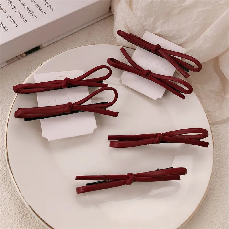 Wine red genuine leather bow hair barrette with a silver metal pinch clip on a white background.