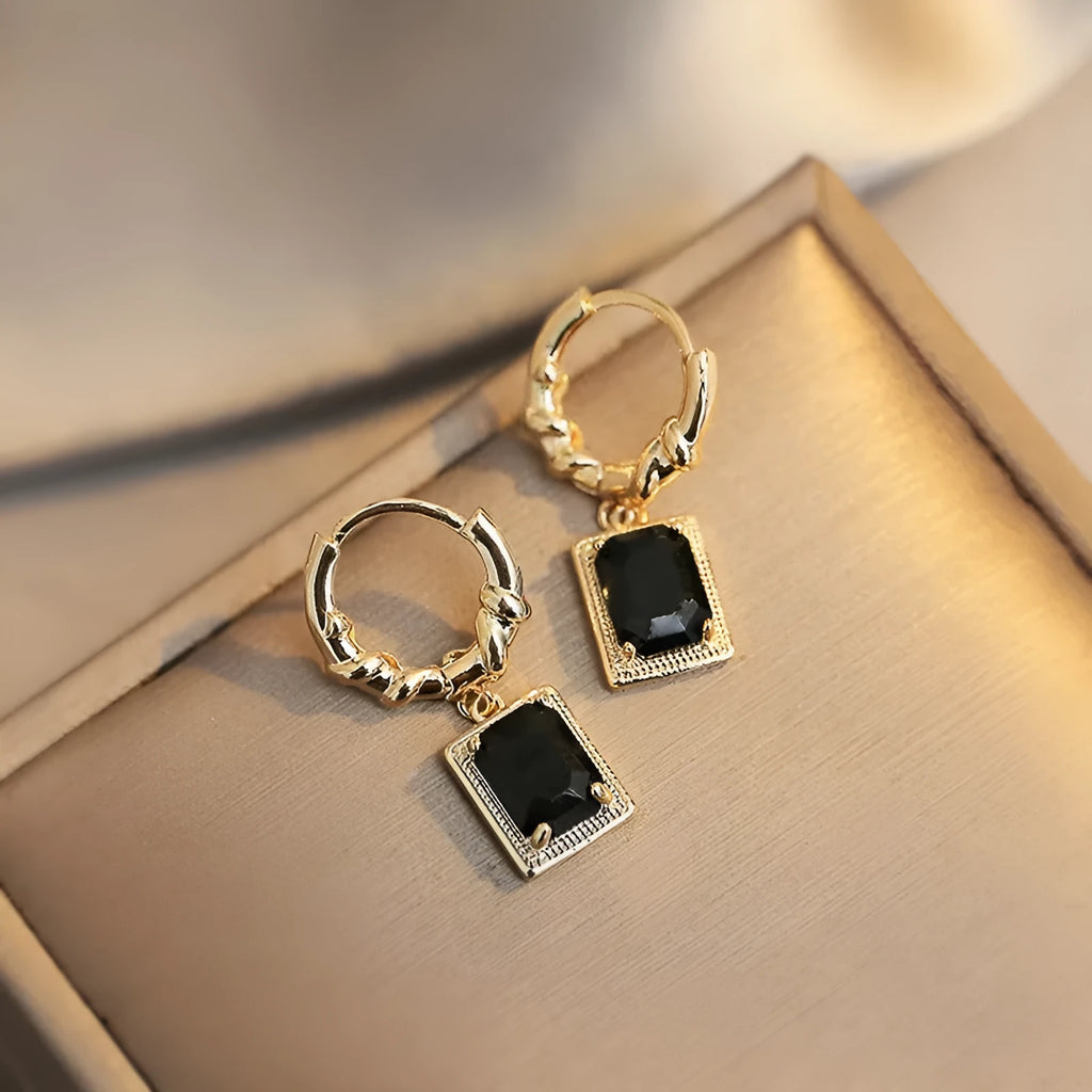 Close-up of women's geometric quadrilateral copper drop earrings with multiple black zircon stones on a grey background.