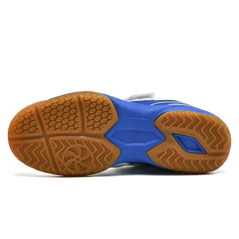 Low-top white and blue badminton shoes with a ribbed sole on a hard court surface.