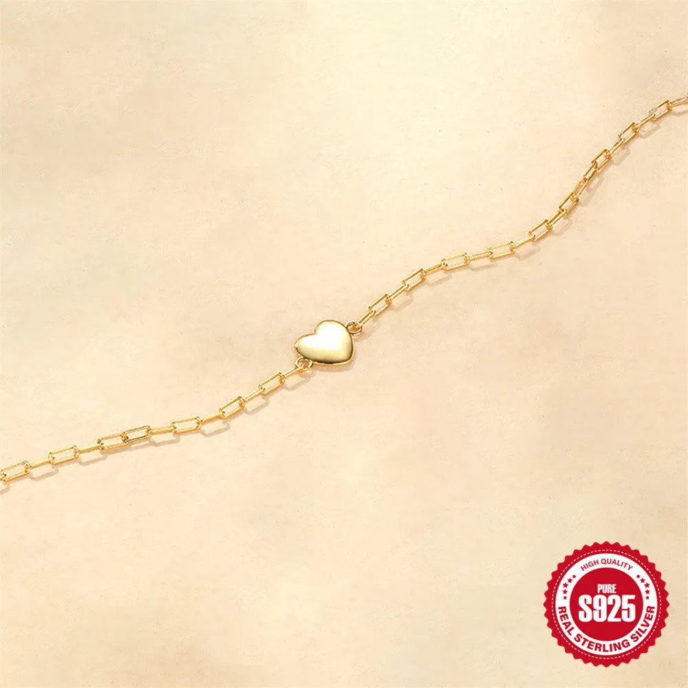 Close-up of a women's sterling silver bracelet with a glossy gold heart charm and lobster clasp.