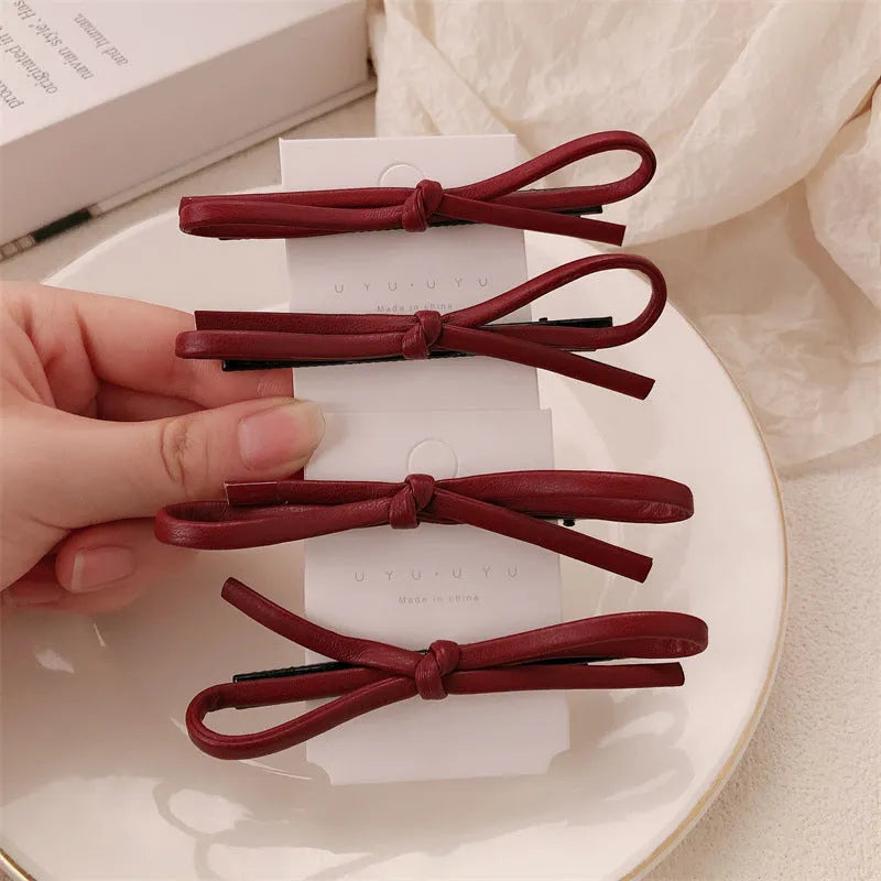 Wine red genuine leather bow hair barrette with a silver metal pinch clip on a white background.