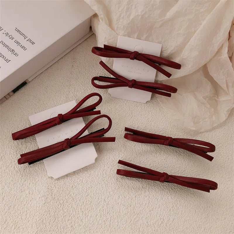Wine red genuine leather bow hair barrette with a silver metal pinch clip on a white background.