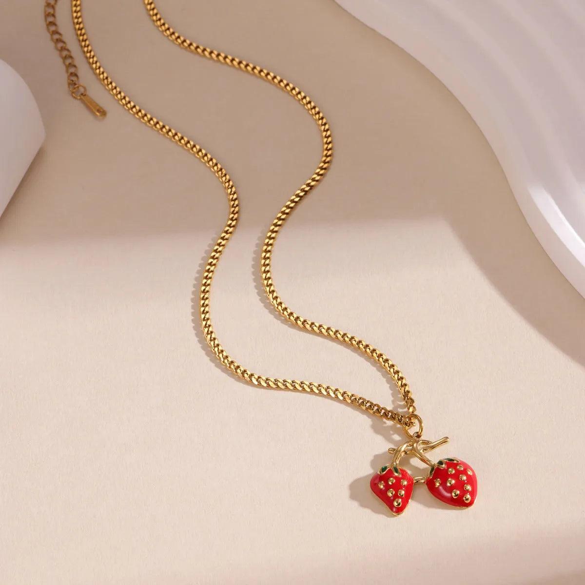 Close-up of a strawberry-shaped alloy pendant necklace on a stainless steel chain, showing red and white colour options.