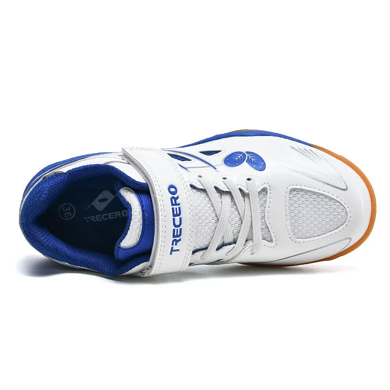 Low-top white and blue badminton shoes with a ribbed sole on a hard court surface.