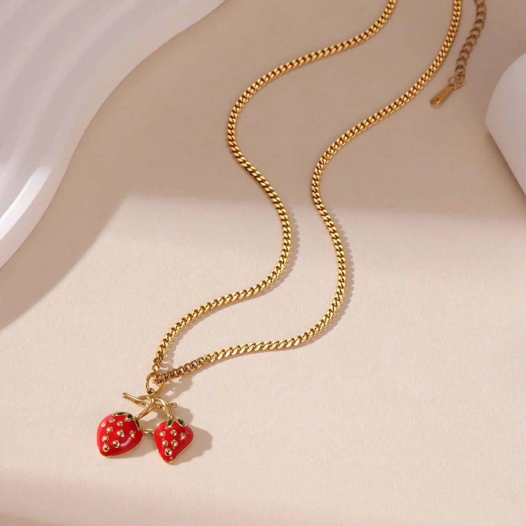 Close-up of a strawberry-shaped alloy pendant necklace on a stainless steel chain, showing red and white colour options.