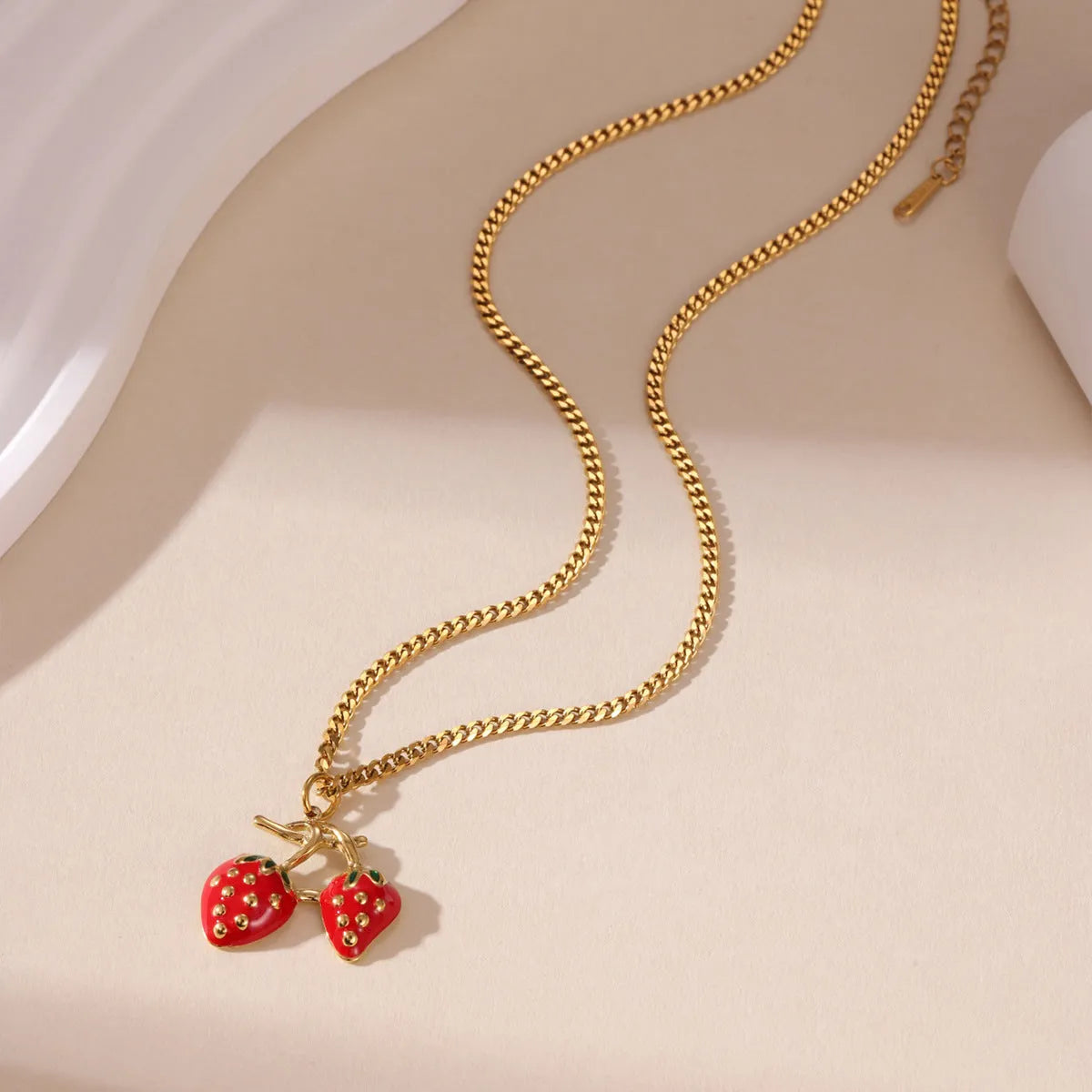Close-up of a strawberry-shaped alloy pendant necklace on a stainless steel chain, showing red and white colour options.