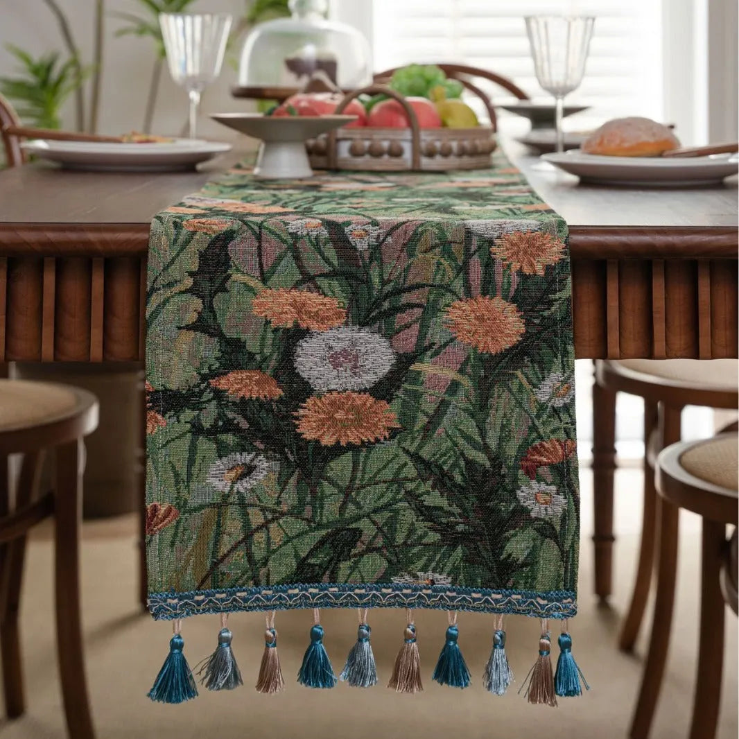 Long beige jacquard table runner with floral pattern and tassels draped on a wooden dining table.