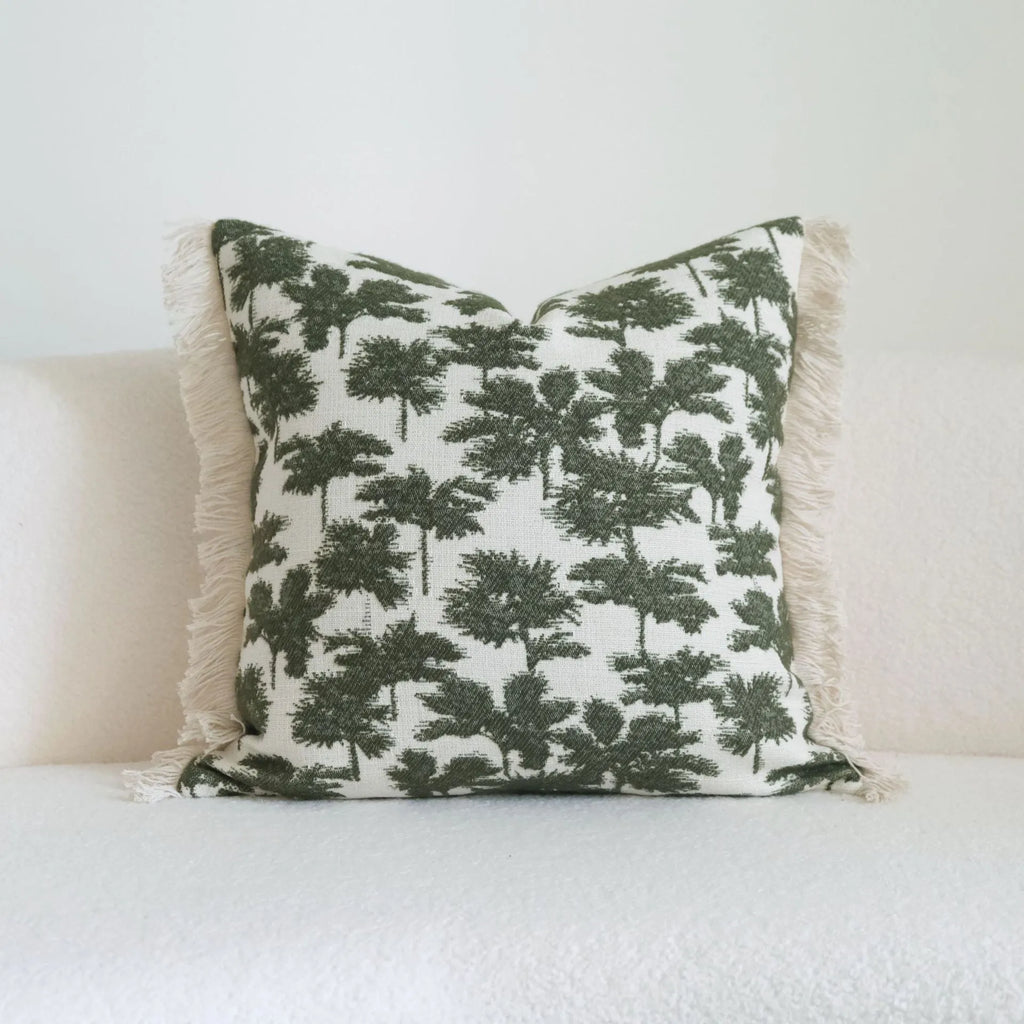 Green striped and botanical patterned pillow with beaded fringe on a bed.