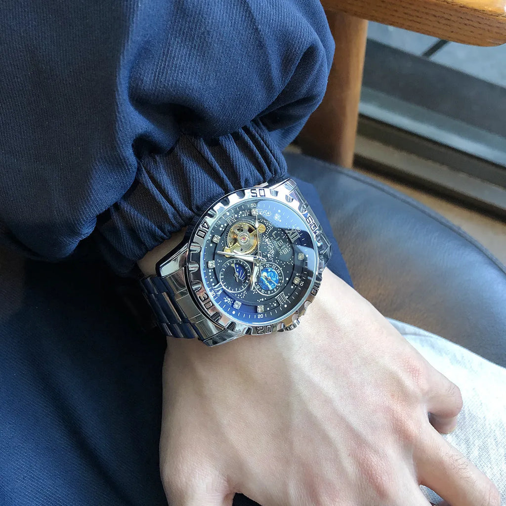 Men's silver automatic watch with black starry dial and leather strap on wrist.
