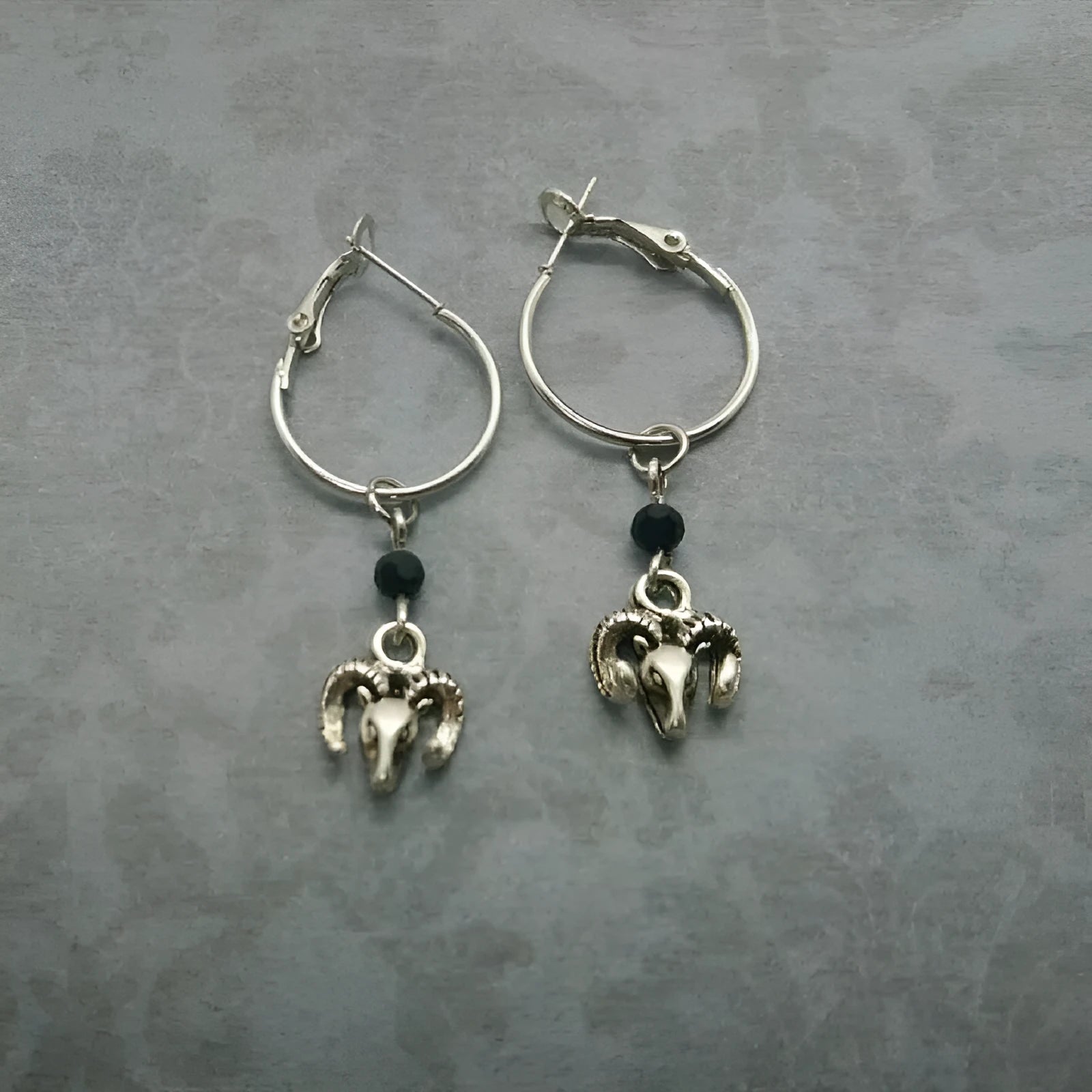 A pair of silver-coloured round ring earrings featuring a detailed Tibetan antelope design.
