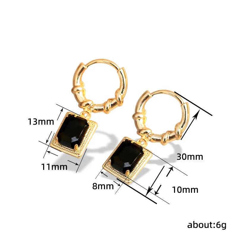 Close-up of women's geometric quadrilateral copper drop earrings with multiple black zircon stones on a grey background.