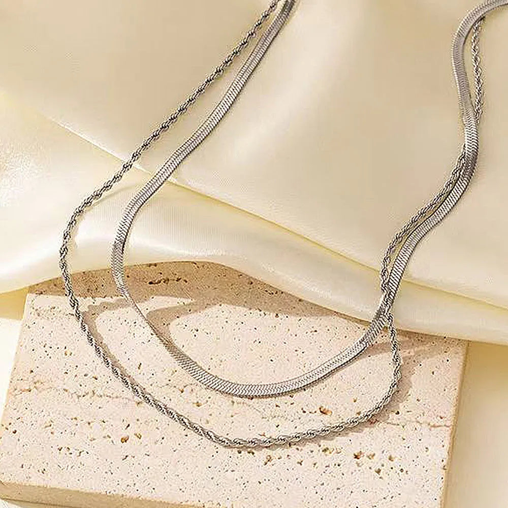Close-up of a women's silver geometric twist necklace on an adjustable snake chain, showing its layered stainless steel pendant.