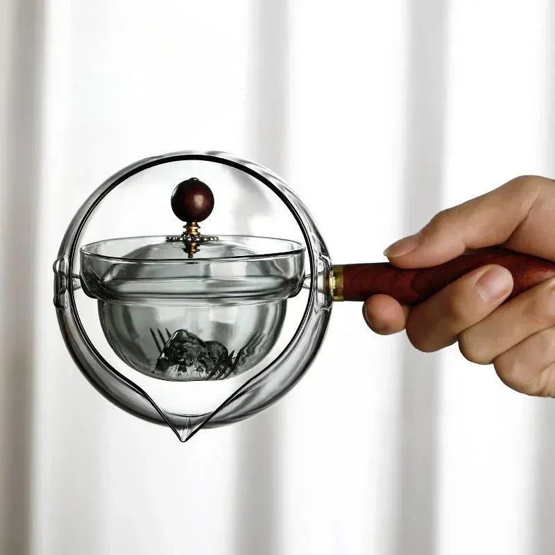 Grey and transparent rotary glass teapot with wooden handle and infuser on a kitchen counter