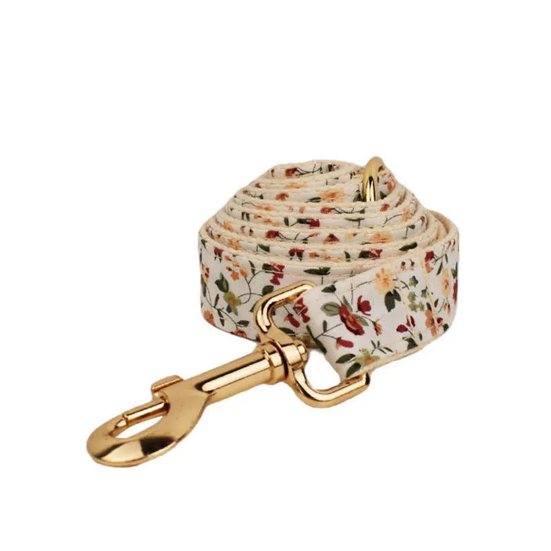 Small white flower pet dog collar set with matching vest, leash, bow, and accessories on a cloth background.