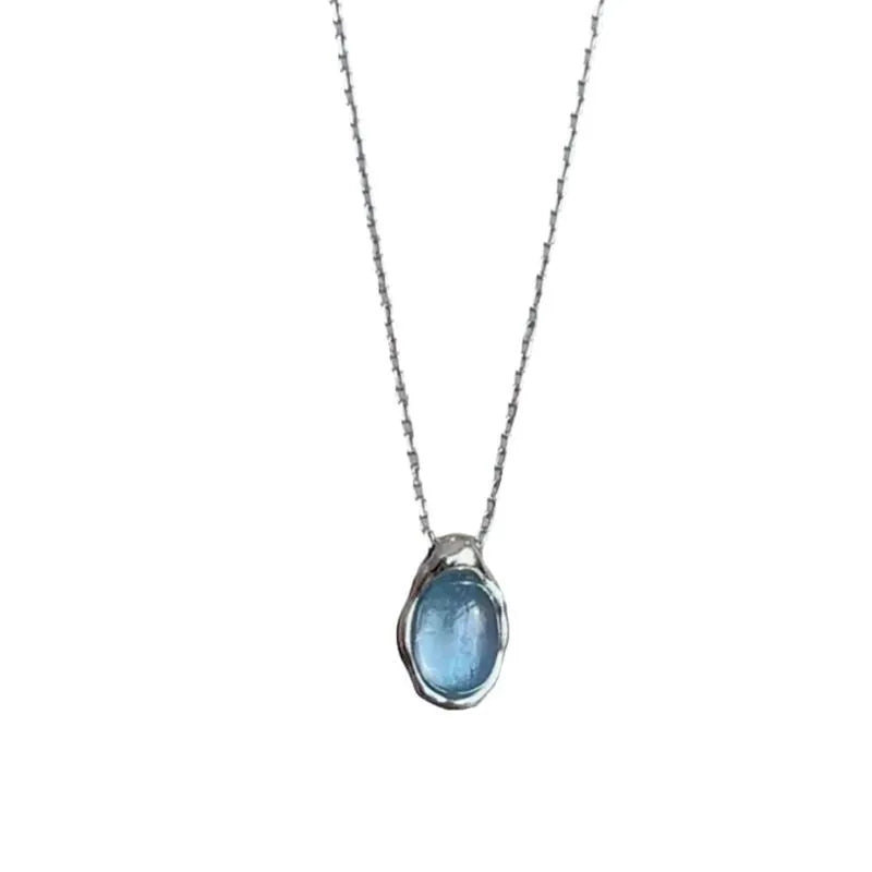 Close-up of a navy blue and platinum coloured water drop pendant necklace with an adjustable cross chain on a person's collarbone.