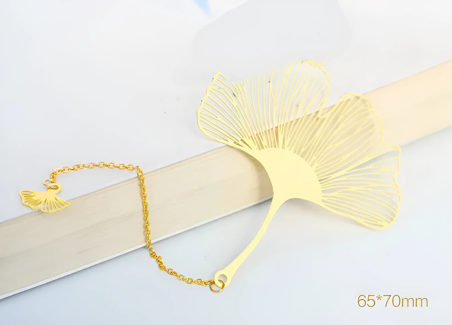 Detailed brass bookmark with hollow maple leaf pendant and rose gold tassel on a book page.