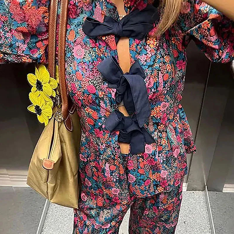 Women's floral print polyester trousers suit with tie-neck blouse and puff sleeves.