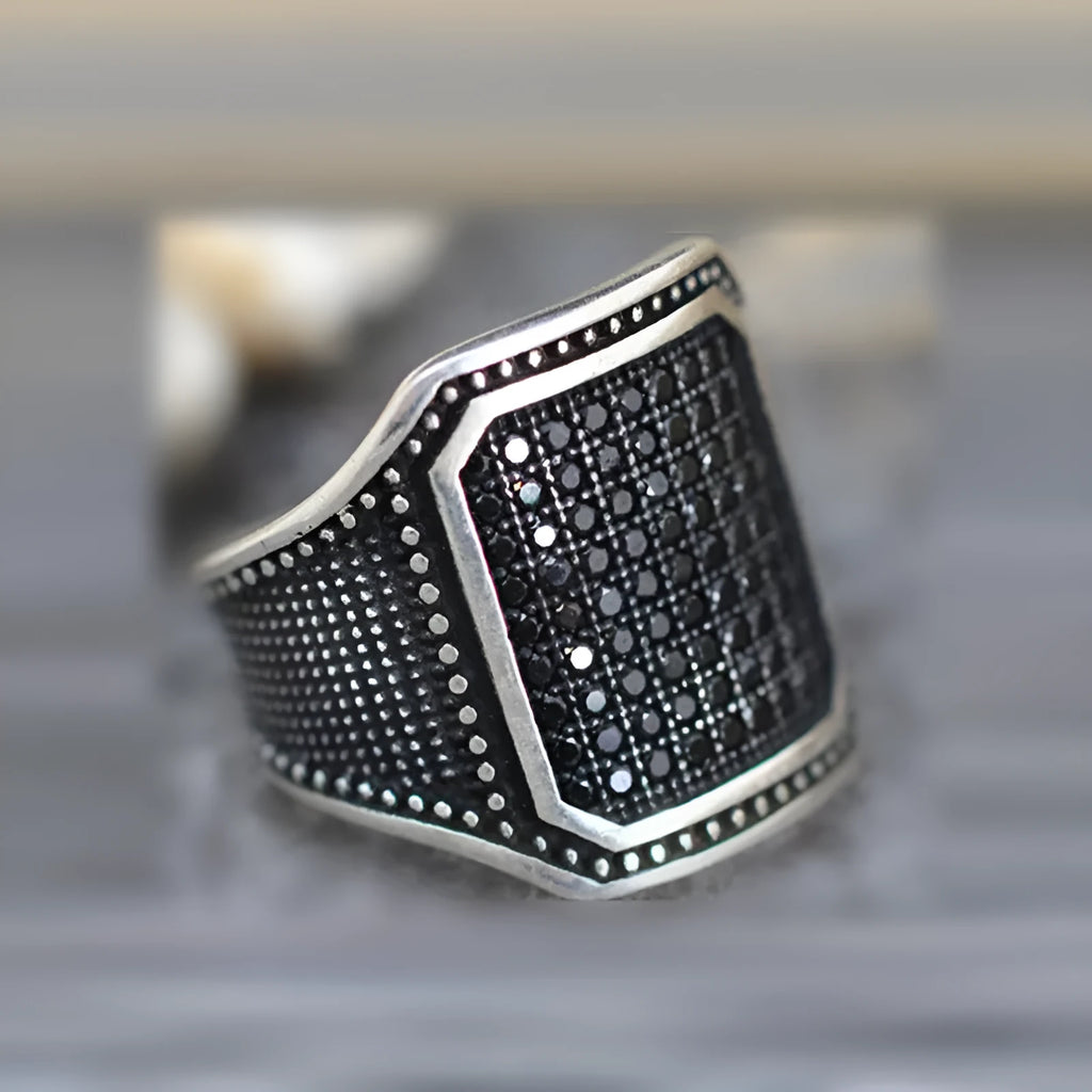 Black alloy ring with inlaid copper detail and a central zircon stone, shown on a finger.