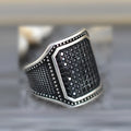 Black alloy ring with inlaid copper detail and a central zircon stone, shown on a finger.