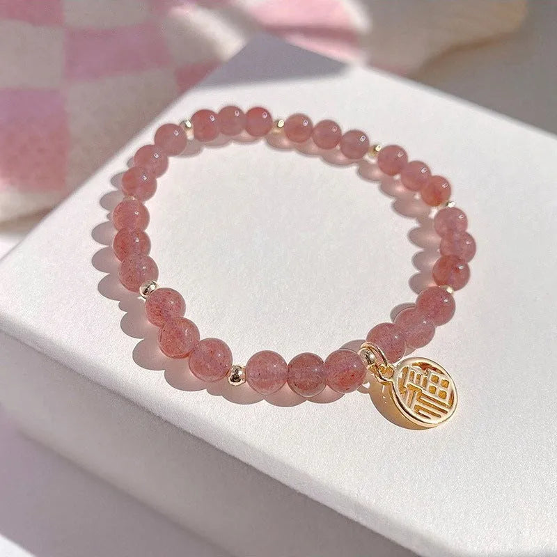 Glass strawberry quartz bead bracelet with a blessing card charm on a wrist.