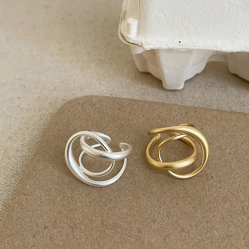 Geometric open ring with a 3D interlaced design in matte gold or silver metal.