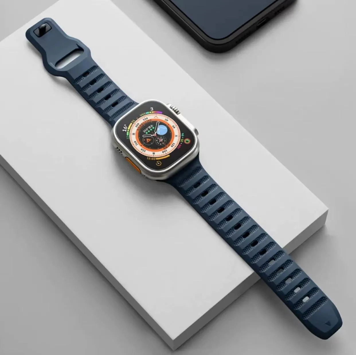 Black fluoro rubber Apple Watch band with T-buckle closure on a wrist, showing compatible Ultra model.