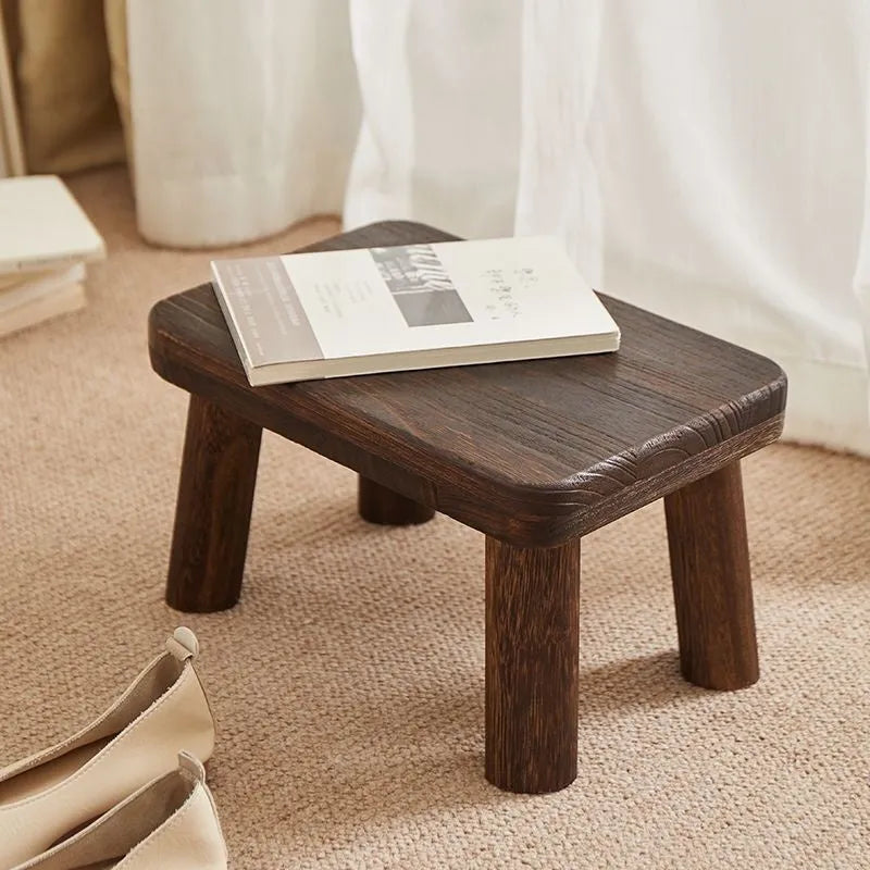 Distressed solid wood shoe changing stool with rustic bracket structure.